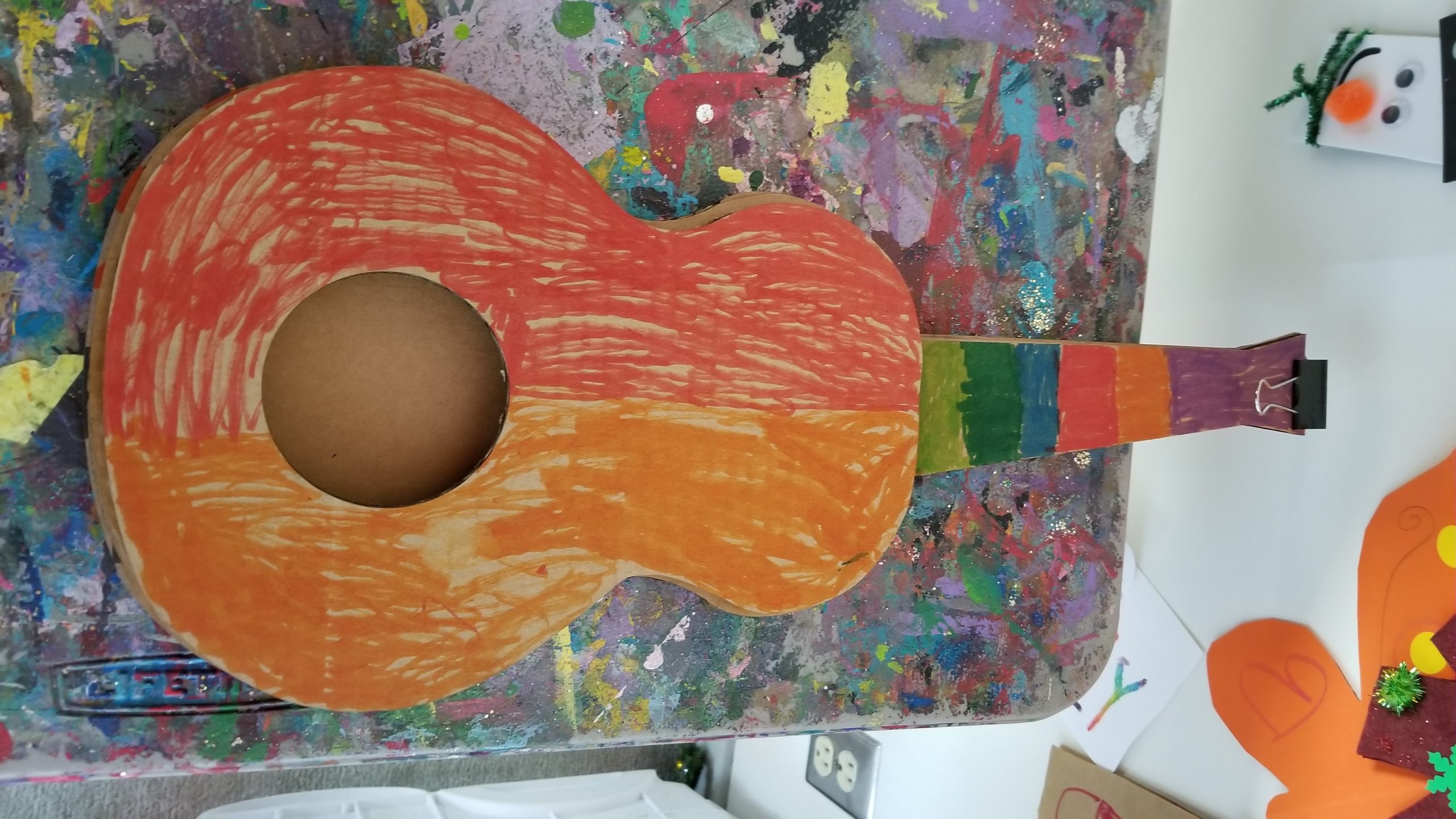 Photo of a cardboard ukulele colored with several colors of marker by a day camper.